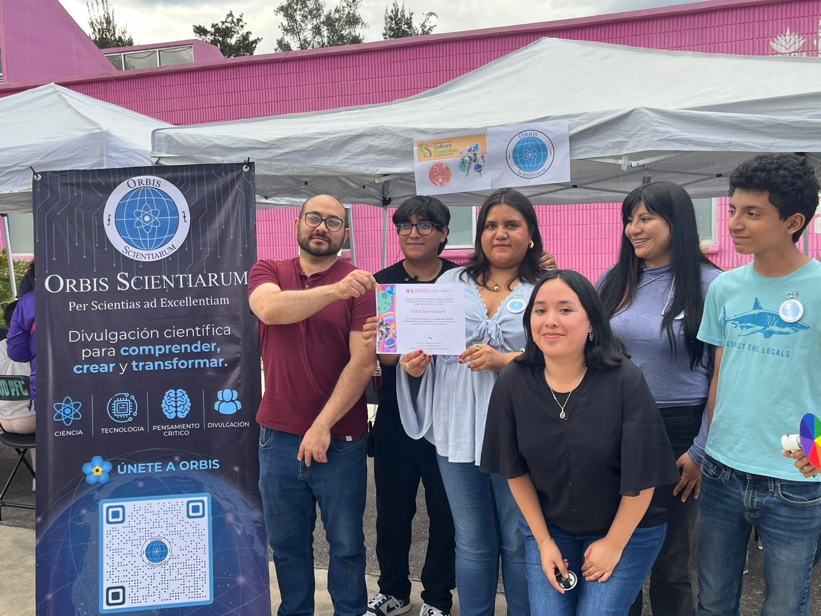 Grupo de miembros de Orbis Scientiarum frente a un estand con el logotipo del colectivo durante una actividad de divulgación.